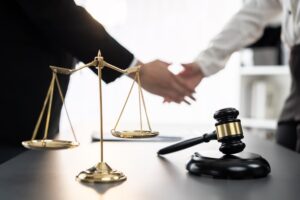 Gavel and justice scale with lawyers shaking hands in the background after a successful legal agreement.