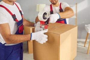 Men workers packing cardboard box with adhesive tape planning to move to a new apartment.