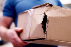 A young mailman carefully carrying a fragile box for delivery accidentally damages it. Protect your items with insurance.