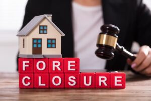 Close-up of a house model and foreclosure blocks in front of a judge with a gavel.