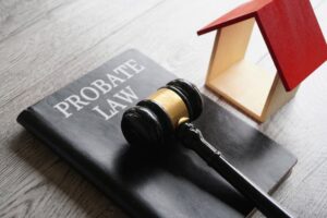 A toy house, a gavel, and the text "PROBATE LAW" are displayed together, symbolizing the intersection of real estate and legal matters in the context of probate law.