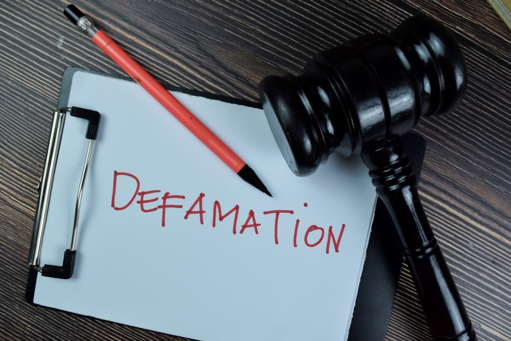 Concept of Defamation write on a paperwork isolated on Wooden Table.