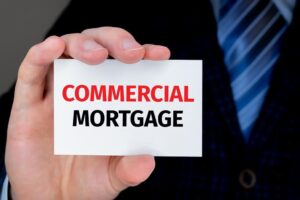 Businessman holding a card with text COMMERCIAL MORTGAGE. Buy and sell