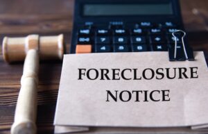 FORECLOSURE NOTICE - words on light brown paper against the background of a calculator and a judge's gavel