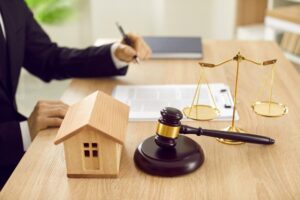 Attorney sitting at desk with scales of justice, gavel and small wooden toy house.